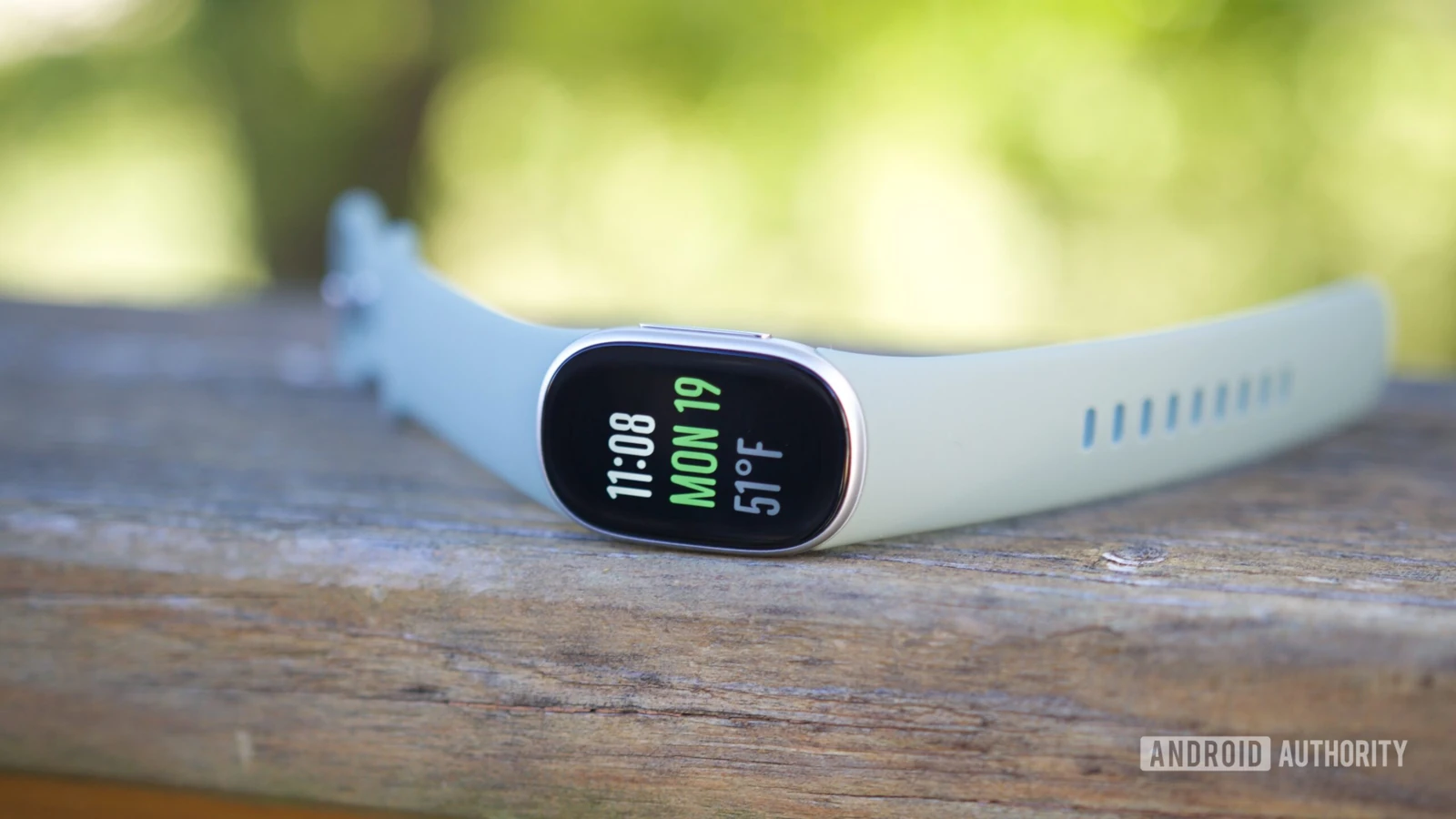 Фитнес-трекер Fitbit Edge со светлым ремешком и включённым экраном лежит на деревянной поверхности на улице