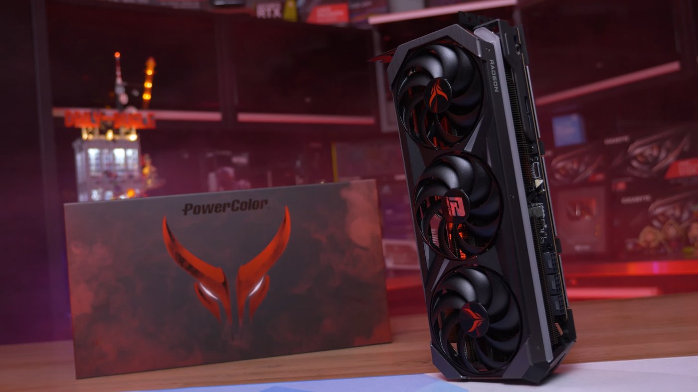 Чёрная видеокарта PowerColor Radeon с тремя вентиляторами стоит рядом с коробкой на столе