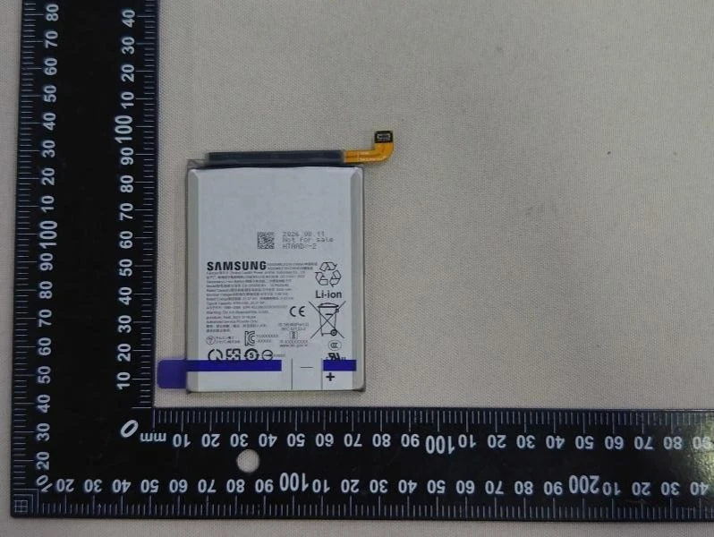 Аккумулятор с маркировкой Samsung и гибким шлейфом лежит рядом с измерительными линейками на сертификационной фотографии